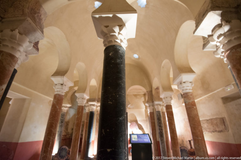 Columned hall with horseshoe arches, red and dark marble shafts, rounded vaults, and small star-shaped ceiling openings.