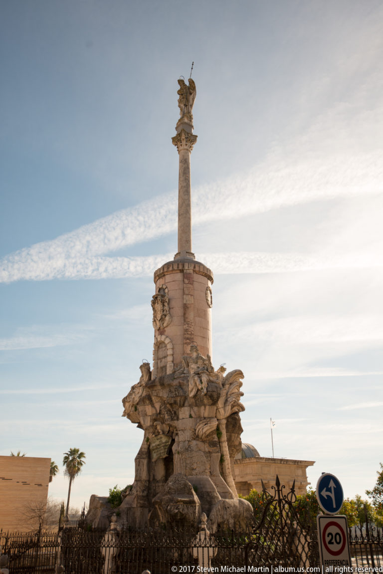Baroque Triunfo de San Rafael with the archangel atop a tall column above a sculptural base and iron enclosure.