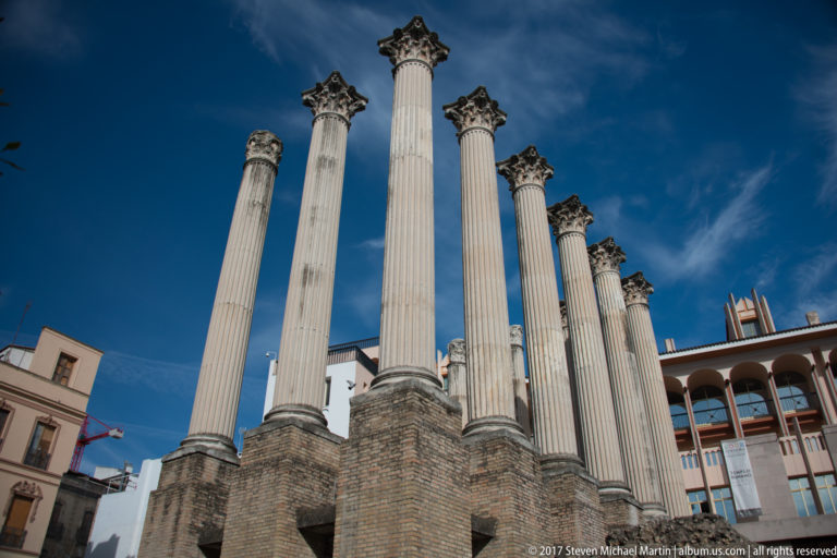 Low-angle view of tall fluted Corinthian columns from Córdoba’s Roman Temple rising above reconstructed bases against blue sky.