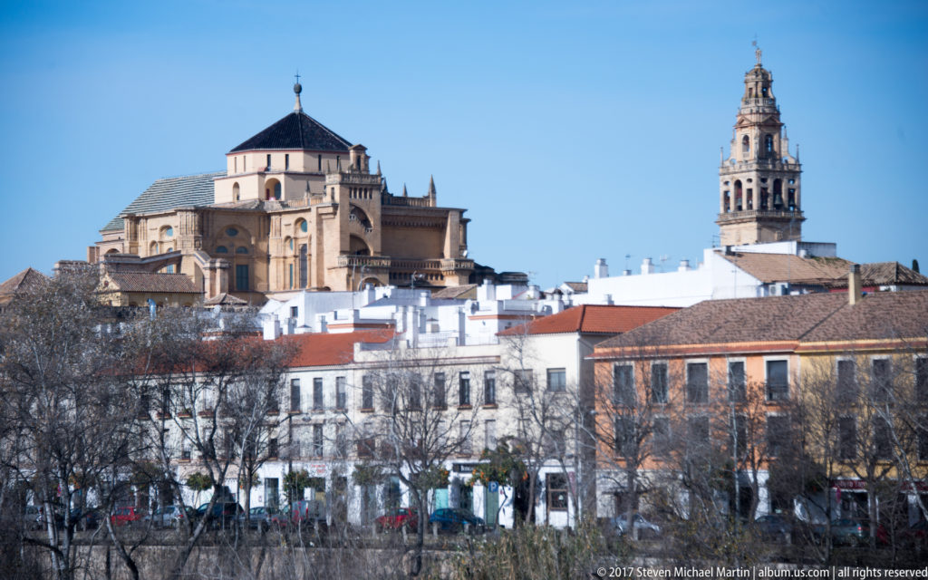 Telephoto skyline view of the Mosque-Cathedral’s cathedral nave and separate bell tower rising above Córdoba’s historic rooftops.