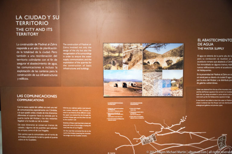 Brown museum panel with bilingual text, archaeological photographs, maps, and headings about territory, communications, and water supply.