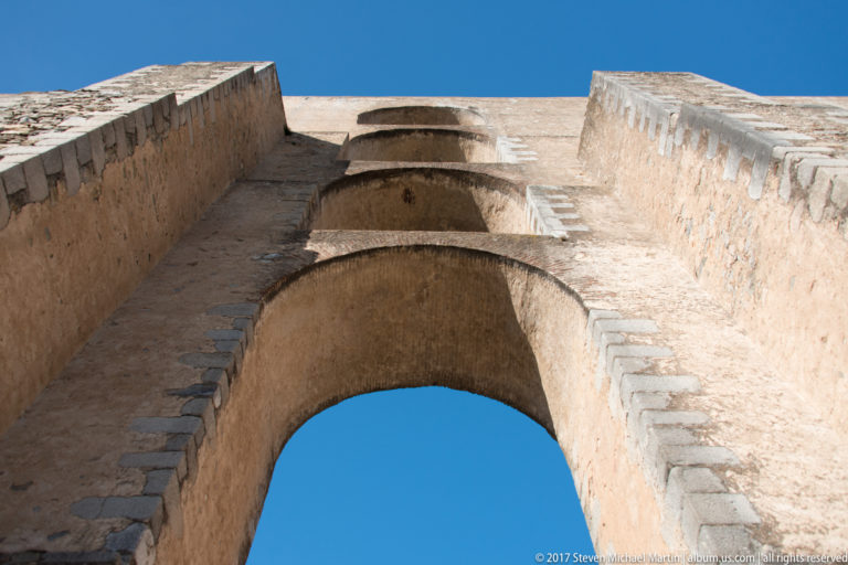 Upward view through a massive round arch of the Amoreira Aqueduct, showing thick masonry against blue sky.