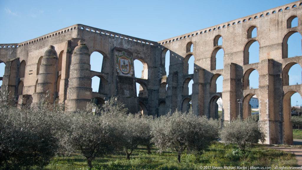Massive buttressed section of the Amoreira Aqueduct with a heraldic panel above tall adjoining arches.