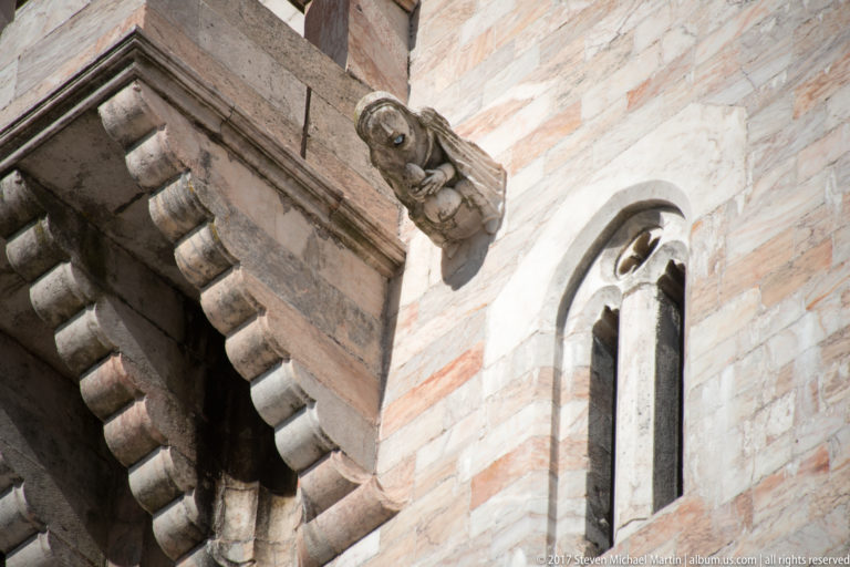 Close view of pale stone keep masonry with a narrow pointed-arched window, projecting corbels, and a carved support.