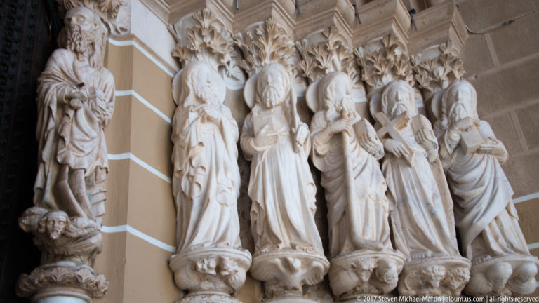 Carved stone apostles beneath Gothic canopies on the west portal of Sé de Évora.