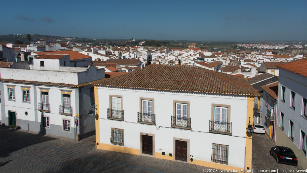 Elevated view across Évora's whitewashed historic center, with red tile roofs and two-story houses in the foreground.