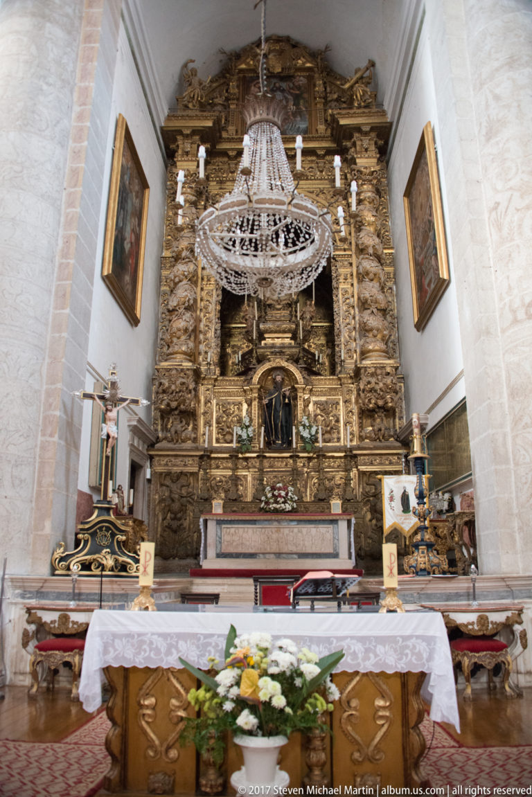 Gilded sanctuary altarpiece and crystal chandelier inside the Igreja de São Francisco in Évora.