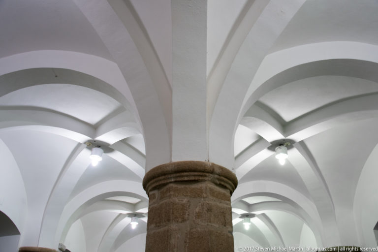White ribbed vaults radiating from a massive granite column in a bright historic hall.