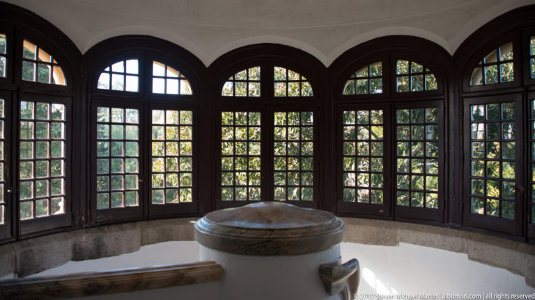 Curved bay of dark wooden multi-pane windows surrounding a low circular stone basin and benches.