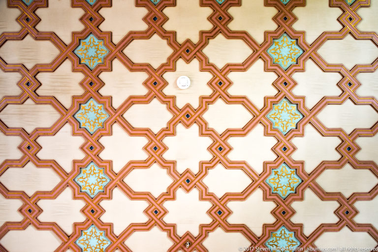 Painted ceiling with interlocking red-brown geometric bands and repeating turquoise-and-gold starburst motifs.