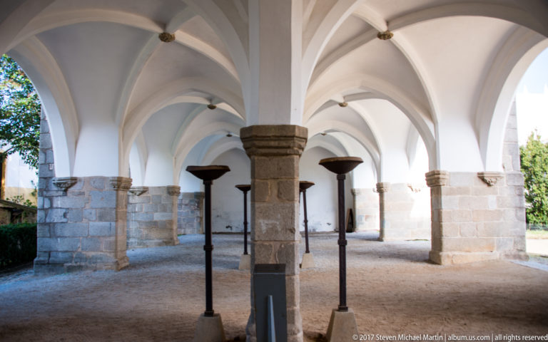 White rib-vaulted arcade supported by heavy granite columns and wall piers, viewed through several repeating bays.