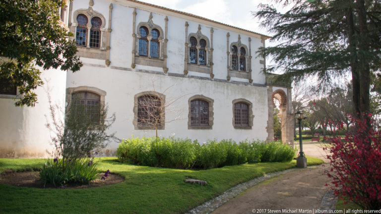 White historic building with ornate upper windows beside a landscaped garden and shaded path in Évora.