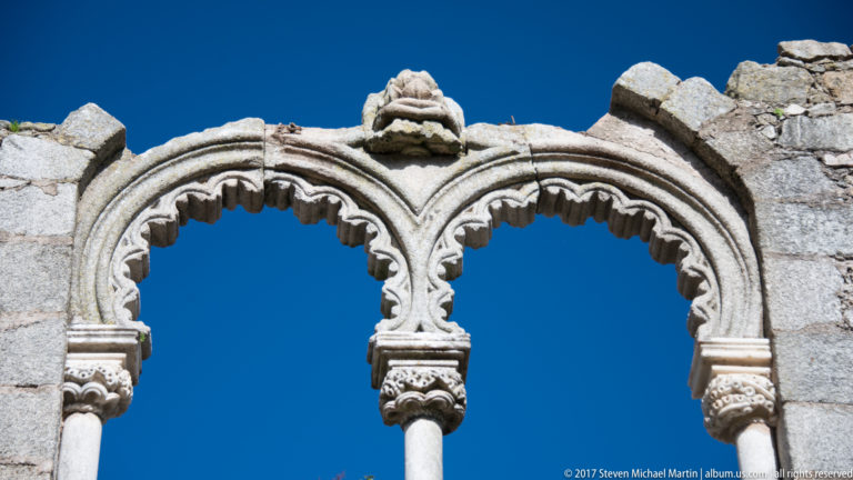 Two ornate lobed stone arches on slender columns silhouetted against a deep blue sky.