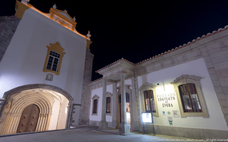Night view of the former Convento dos Lóios, now Pousada Convento de Évora, with its tower, stone entrance, and colonnaded wing.