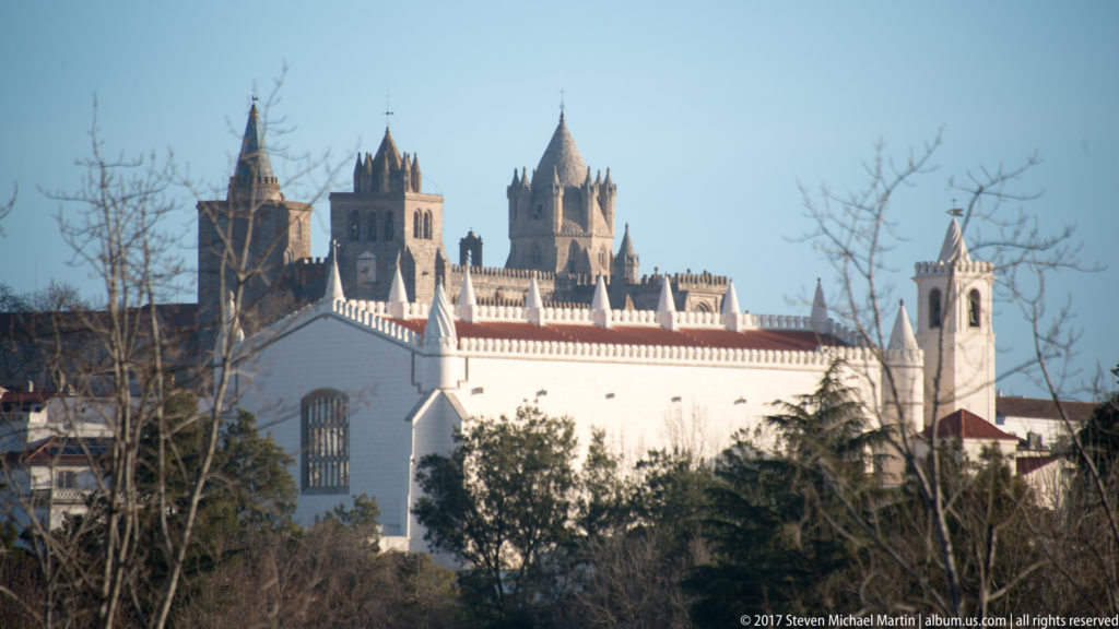 Évora Cathedral towers rising behind a white historic complex with crenellated roofline and bell tower.