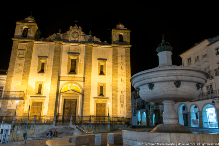 Church of Santo Antão and marble fountain together in Praça do Giraldo at night, with arcaded buildings behind.