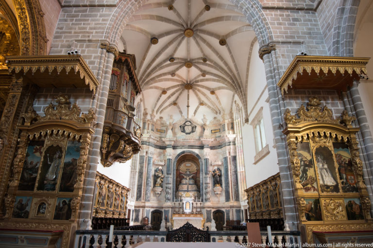 Church interior with two ornate polychrome retables flanking a pale marble sanctuary beneath ribbed vaults in the Igreja de São Francisco complex in Évora.