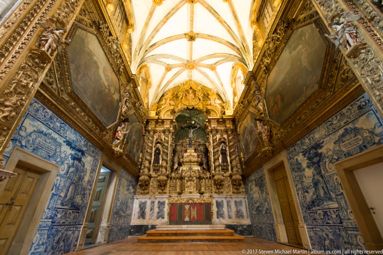 Baroque chapel with blue-and-white azulejo walls, large paintings, gilded retable, marble steps, and ribbed vault in the Igreja de São Francisco complex in Évora.