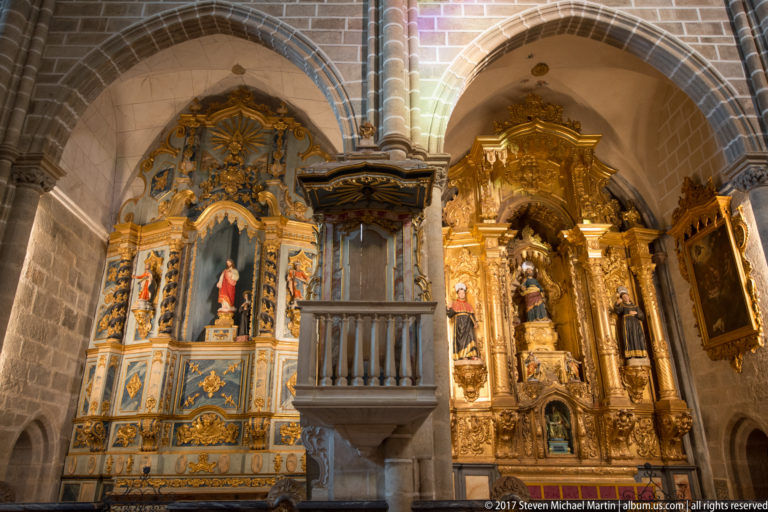 Two ornate side altars and a projecting stone pulpit beneath Gothic arches in an Évora church interior in the Igreja de São Francisco complex in Évora.