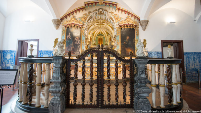 Ornate chapel with blue-and-white tile walls, dark balustrade, large paintings, sculpture, and a gilded altar in the Igreja de São Francisco complex in Évora.