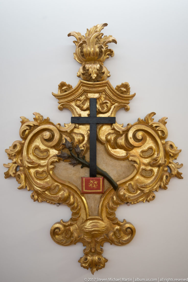 Black cross and small red reliquary element mounted on an elaborate gilded Rococo-style decorative frame in the Igreja de São Francisco complex in Évora.