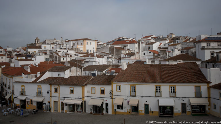 Elevated view across Évora's whitewashed historic center with red roofs, ochre-trimmed buildings, and church towers.
