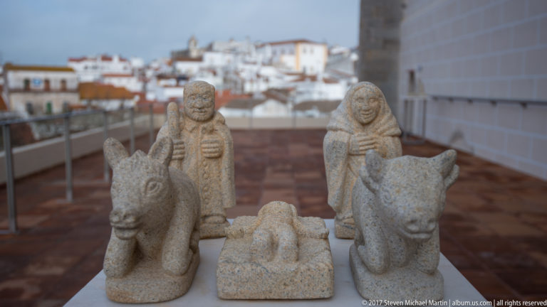 Small weathered stone Nativity group with Mary, Joseph, infant Jesus, ox, and donkey overlooking Évora.