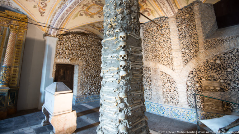 Skull-studded bone-covered pier beside a pale burial monument inside Évora's Chapel of Bones.