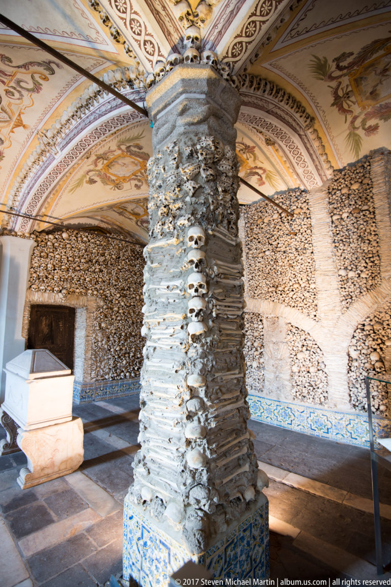 Large pier covered with stacked human long bones and skulls beneath painted vaults in Évora's Chapel of Bones.