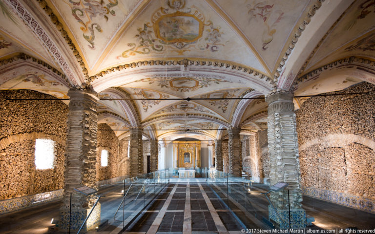 Long symmetrical view through Évora's Chapel of Bones, with bone-covered walls and piers beneath painted vaults.