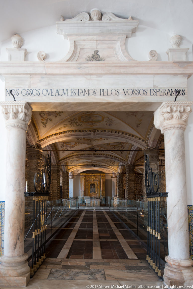 Entrance to Évora's Chapel of Bones with Portuguese inscription above marble columns and the bone-lined interior beyond.