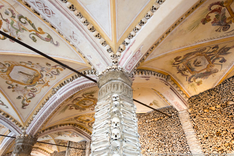 Bone-covered piers and walls rising to painted vaults edged with skulls inside Évora's Chapel of Bones.