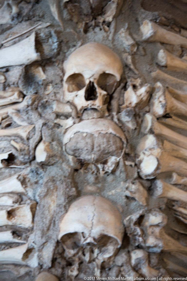 Close view of two human skulls embedded among densely packed bones in the wall of Évora's Chapel of Bones.