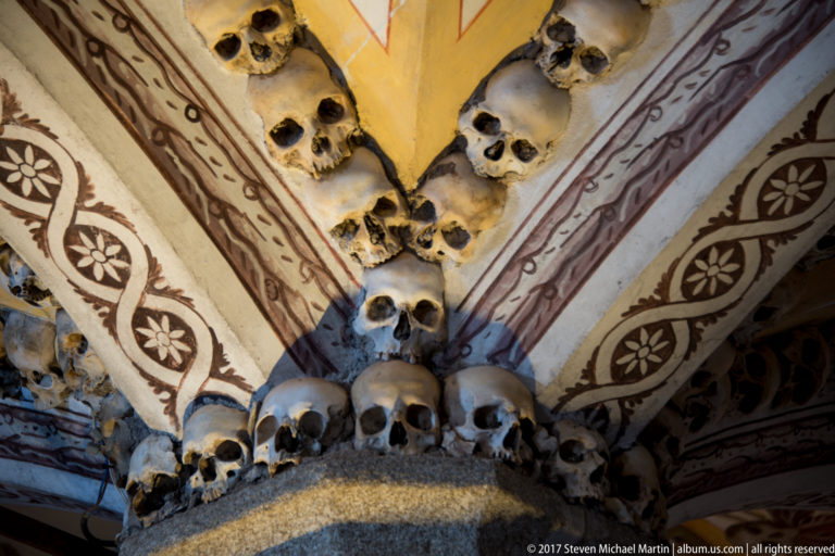 Human skulls lining painted vault ribs and clustering around a pier inside Évora's Chapel of Bones.