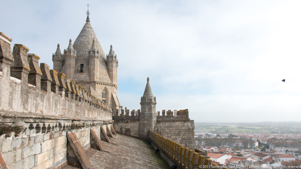 Évora Cathedral rooftop parapet and tower overlooking the red-roofed city and distant Alentejo landscape.
