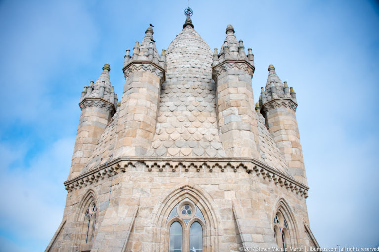Low-angle close view of Évora Cathedral's polygonal central tower with pointed windows, corner turrets, and patterned conical roof.
