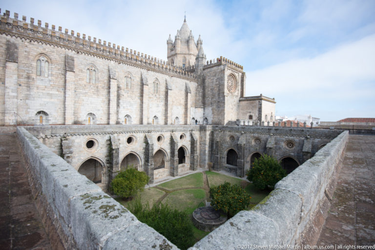 Elevated view over Évora Cathedral cloister garden toward the long buttressed cathedral wall and tall rooftop tower.
