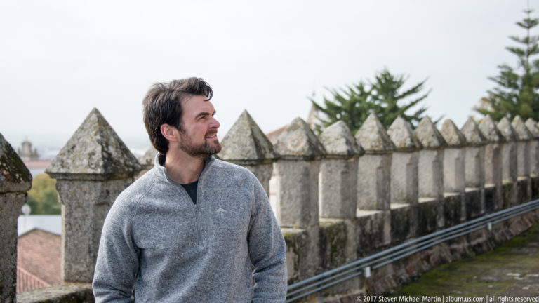 Visitor standing beside the pointed stone crenellations of Évora Cathedral's rooftop walkway.