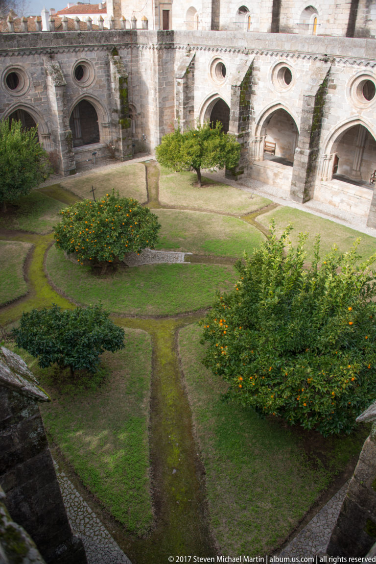 Elevated view into Évora Cathedral's cloister garden with citrus trees, paths, flower beds, and surrounding Gothic arcade.