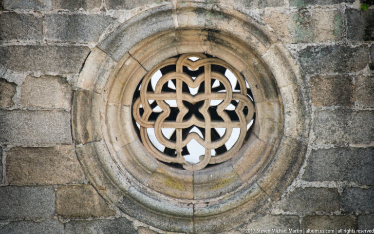 Circular stone window with looping floral-geometric tracery surrounded by concentric moldings in weathered masonry.
