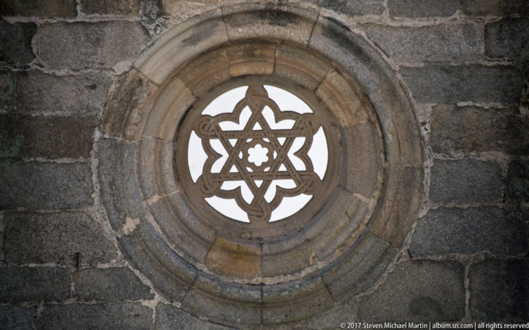 Circular stone window with interlaced geometric tracery and a small central rosette set in dark masonry.