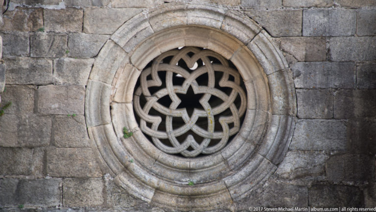 Circular stone window with interlaced tracery and a star-shaped center set in rough gray ashlar masonry.