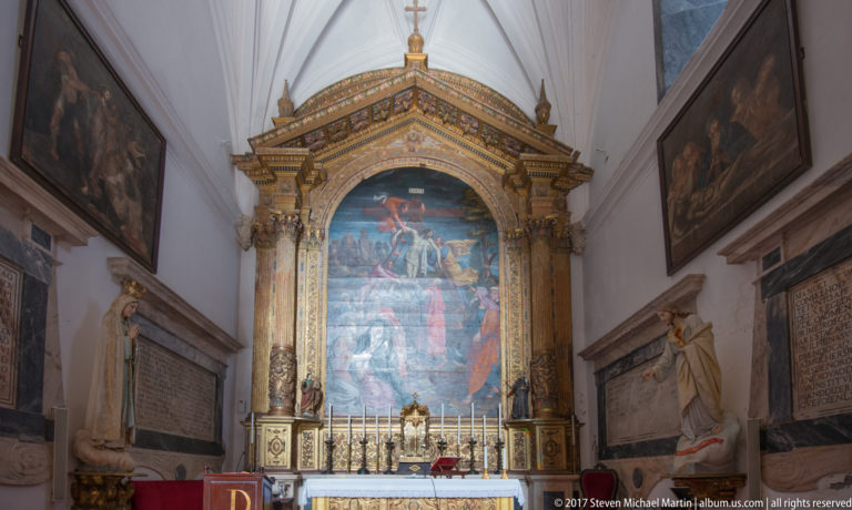 Side chapel with a large Crucifixion painting in a gilded frame above an altar, flanked by sculpted figures.