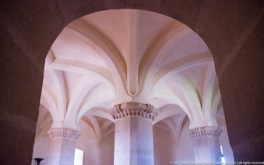 Pale rib vaults rise from thick stone columns with carved capitals inside Evoramonte Castle.
