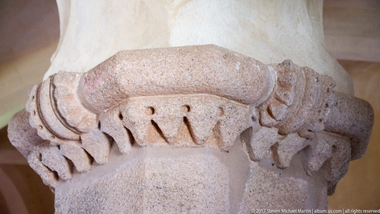 Close view of a weathered stone capital carved with pointed leaf-like motifs beneath a vault spring.