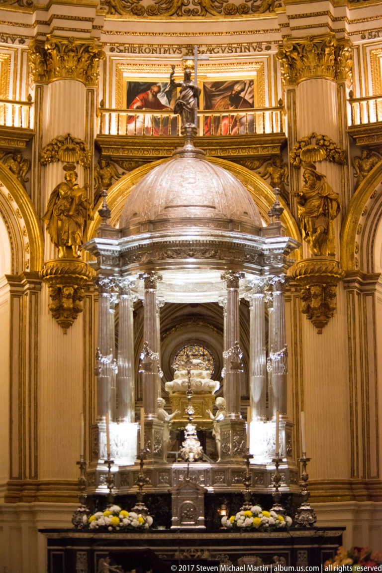 Domed silver-toned sanctuary pavilion with slender columns, candles, and flowers in Granada Cathedral's Capilla Mayor.