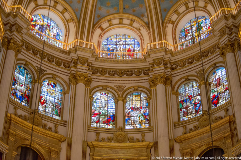 Series of colorful stained-glass windows around the curved upper wall of Granada Cathedral's Capilla Mayor.