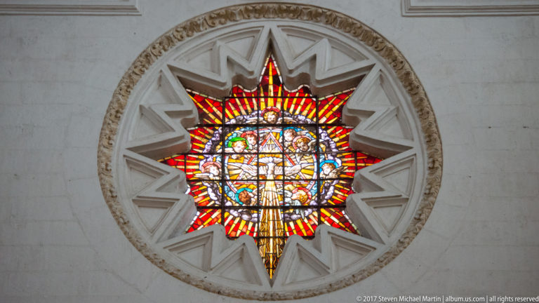 Colorful circular stained-glass window with red-and-yellow rays inside a star-shaped pale stone surround.