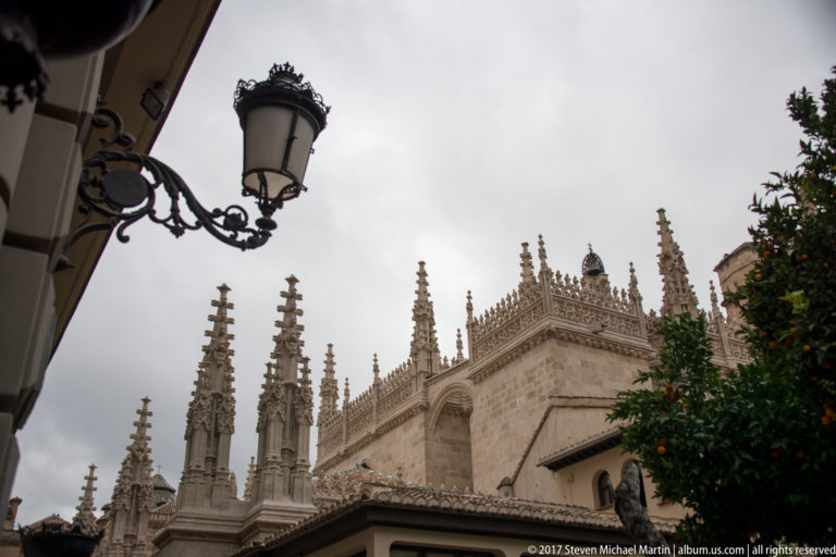 Stone pinnacles and upper walls of Granada Cathedral framed by a street lantern and orange tree.