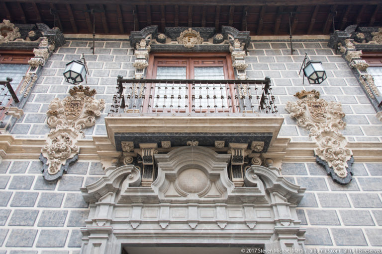 Wooden balcony surrounded by elaborate carved stone ornament on a rusticated historic façade in Granada.